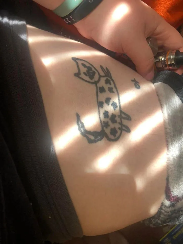 Tattoo of a simple doodle cat with spots on a person’s skin, illustrating a poorly executed tattoo design.