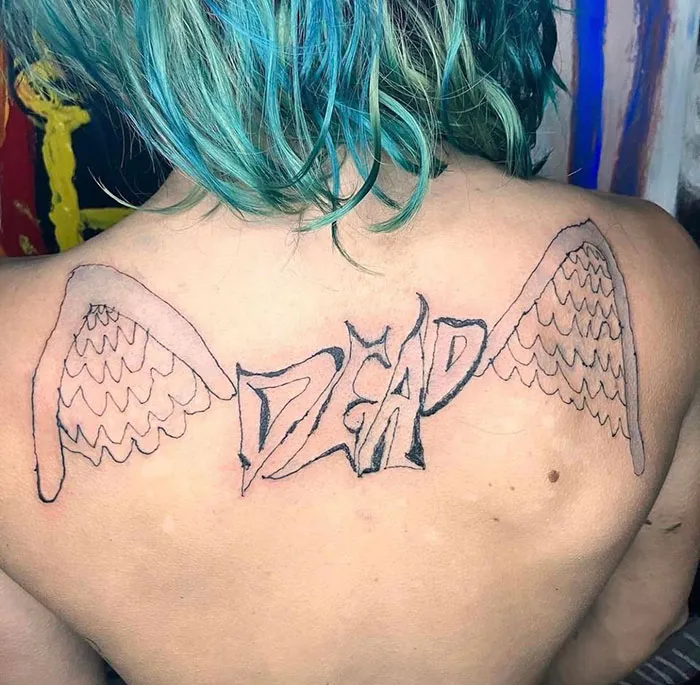 Person with a poorly designed tattoo of wings and the word "dead" on their back, highlighting bad tattoo art.
