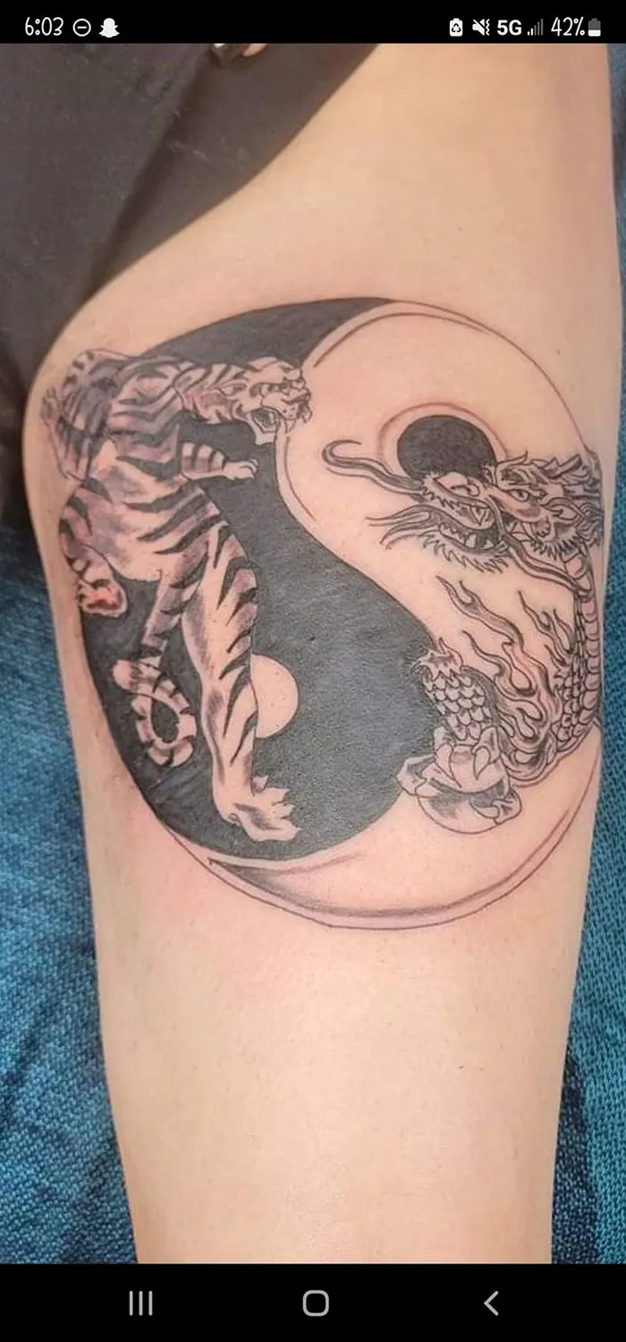 Bad tattoo of a tiger and dragon in yin-yang design on a person's arm.