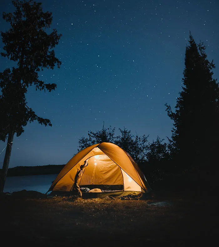 Night camping scene with tent glowing under starlit sky, a perfect solo activity for “me time.”