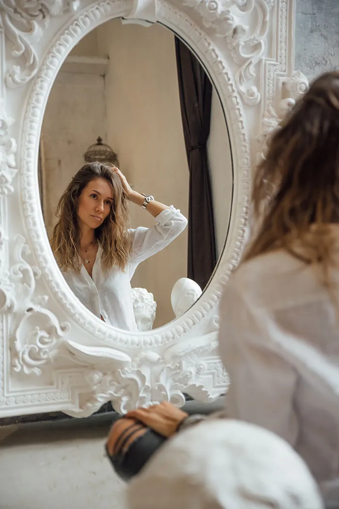 Woman enjoying me time, looking in ornate mirror.