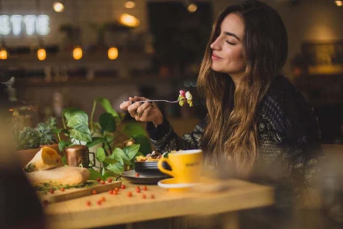 Woman enjoying a meal alone, smiling with a fork in hand, promoting the concept of "me time."