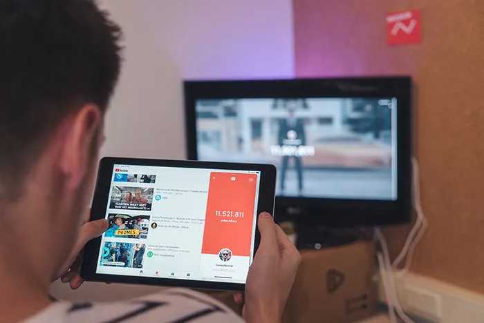 Person enjoying "me time" watching videos alone on a tablet, with a TV in the background.