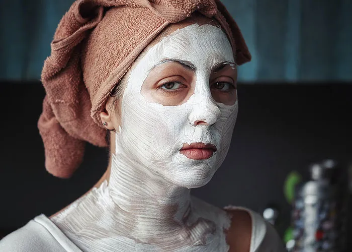 Person enjoying me time with a face mask, towel wrapped around hair, in a relaxed setting.