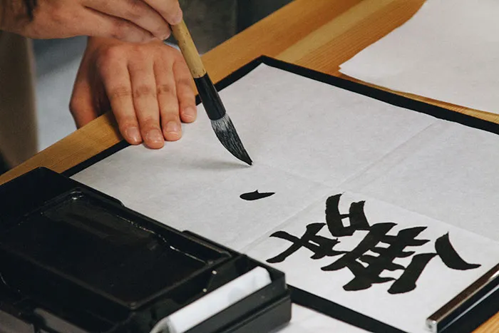 Person practicing calligraphy alone on a wooden table with ink and brush, focusing on personal time.