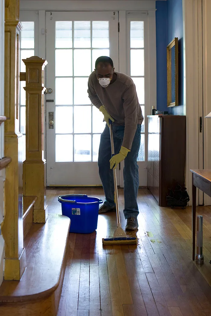 Person mopping wooden floor, enjoying some me time while cleaning the house, with a blue bucket nearby.