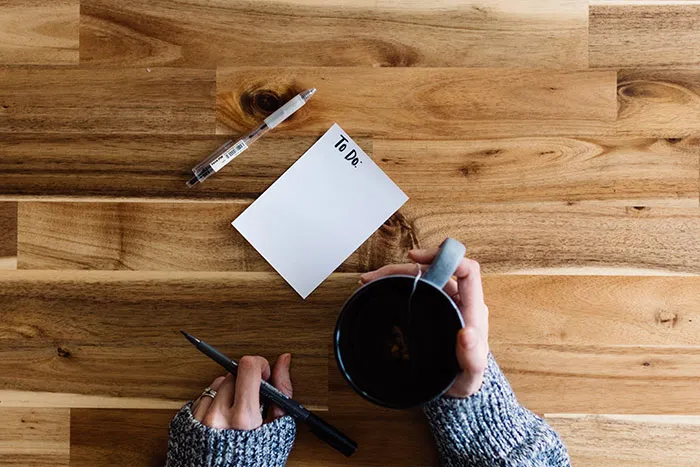 Person enjoying tea, contemplating activities for alone time with a to-do list, pen, and wooden table setting.