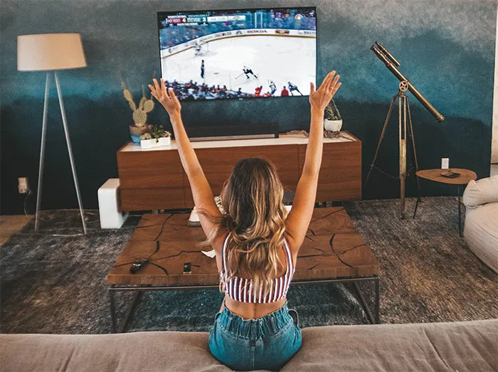 Woman enjoying me time watching a sport game on TV, raising her arms in excitement.
