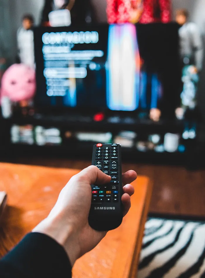 Person relaxing with TV remote during me time, enjoying a solo movie or show.