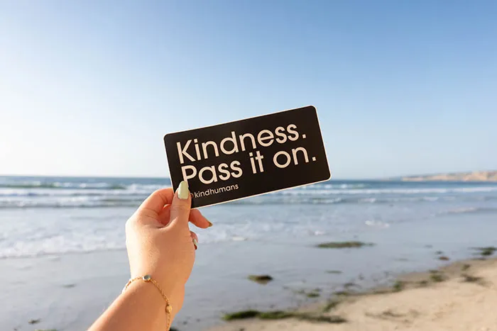 Person holding a card with "Kindness. Pass it on." message, ideal for solo reflection during "me time."