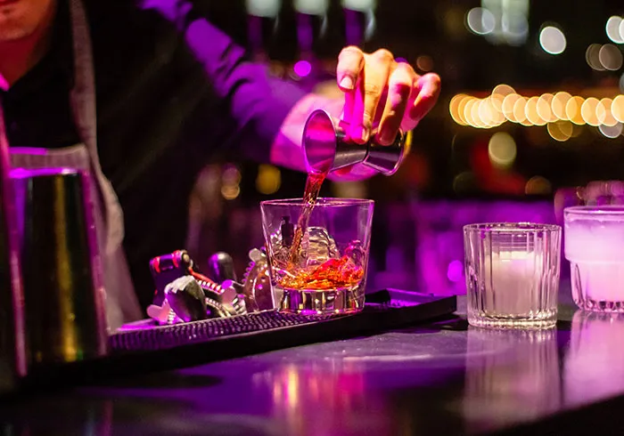 Person enjoying me time by making a cocktail at a bar, illuminated by warm lights.