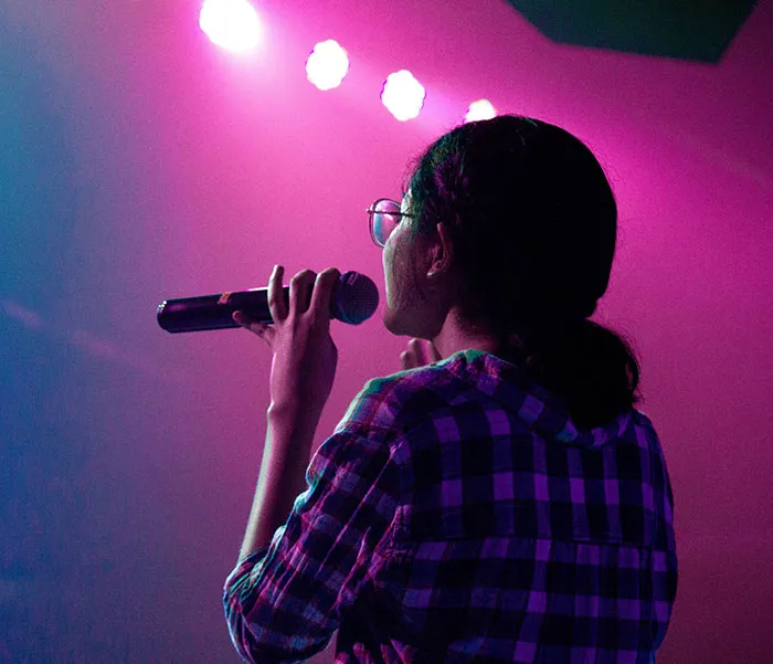 Woman enjoying karaoke singing under pink lights, embracing some "me time."