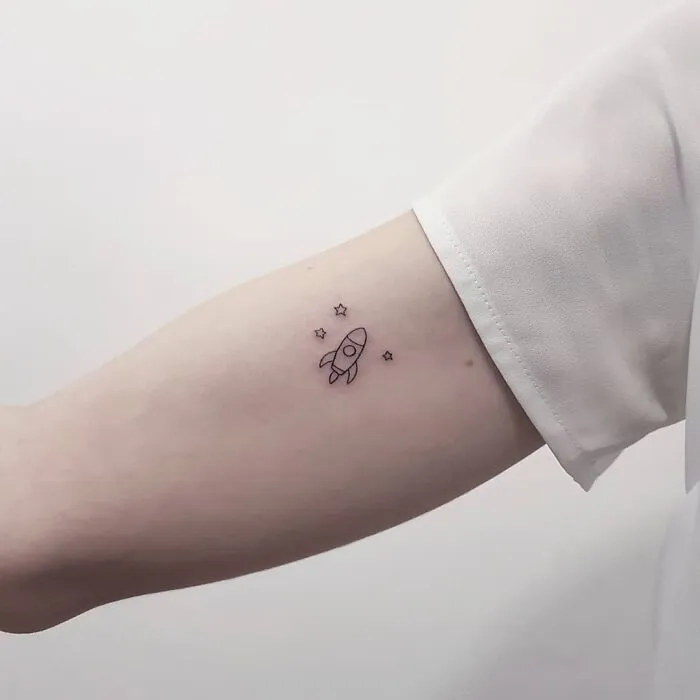 Minimalist tattoo of a rocket and stars on an arm, showcasing aesthetically pleasing design.