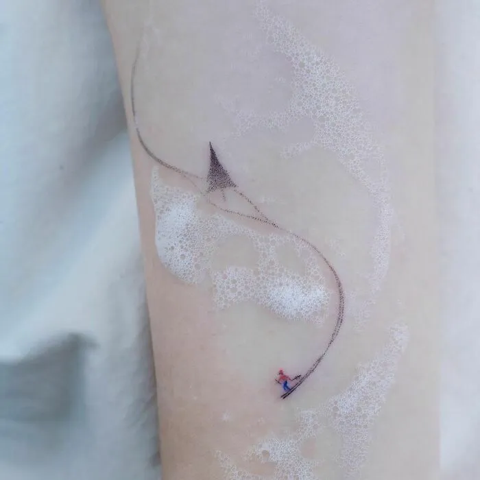 Minimal tattoo design of a delicate kite flying across the skin with bubbles.