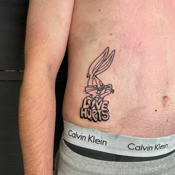 Cartoon tattoo of a classic animated character with "Love Hurts" text on a person's side torso.