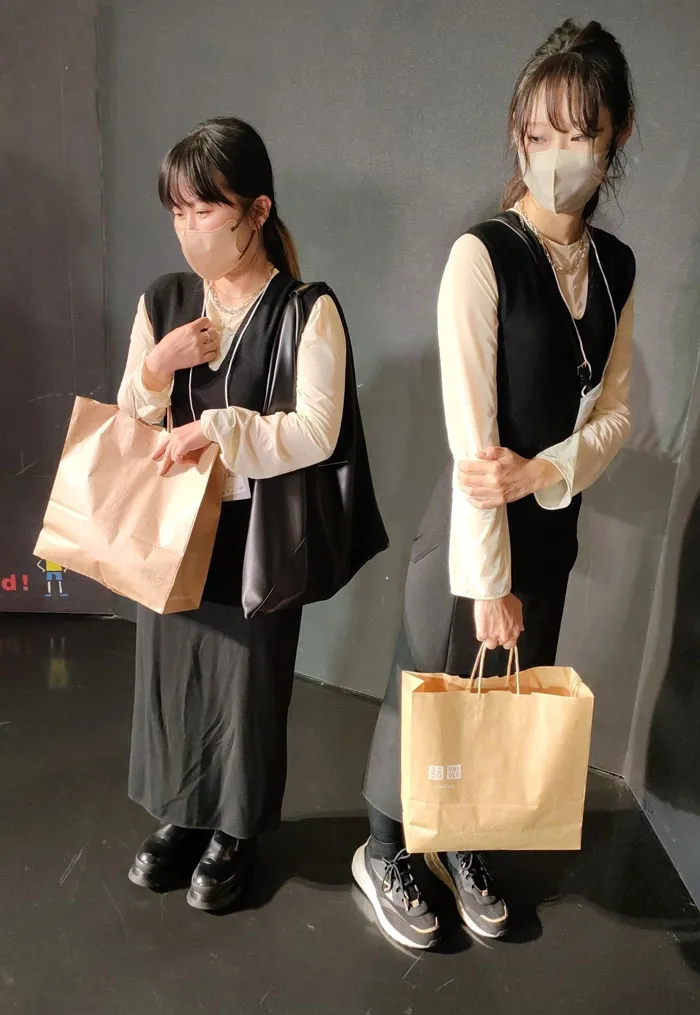 Two people in black and beige outfits with face masks, holding brown bags, showcasing mundane Halloween costumes.