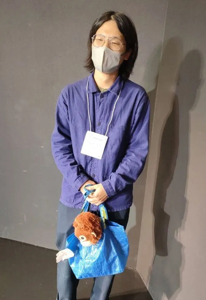 Person in a mask wearing a blue shirt, holding a blue bag with a toy, embodying a mundane Halloween costume.