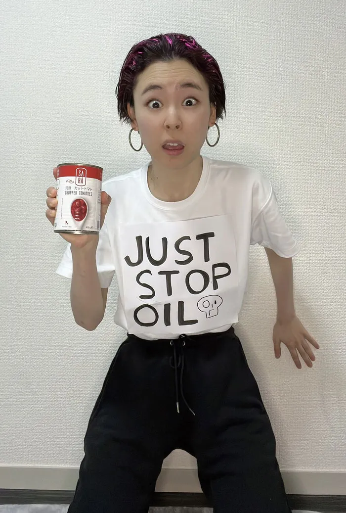 Person in "Just Stop Oil" shirt holding can, showcasing Mundane Halloween costume with a surprised expression.