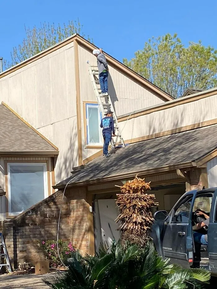 Two workers on a ladder over a rooftop, seemingly ignoring OSHA safety regulations.