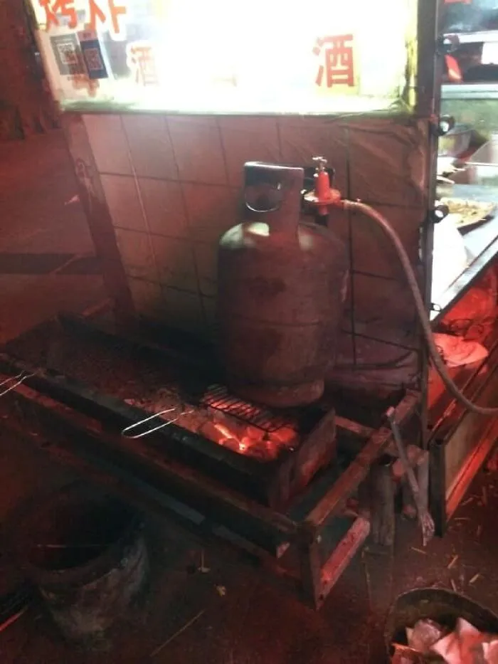 Propane tank sits precariously close to grill, showcasing disregard for OSHA safety regulations.