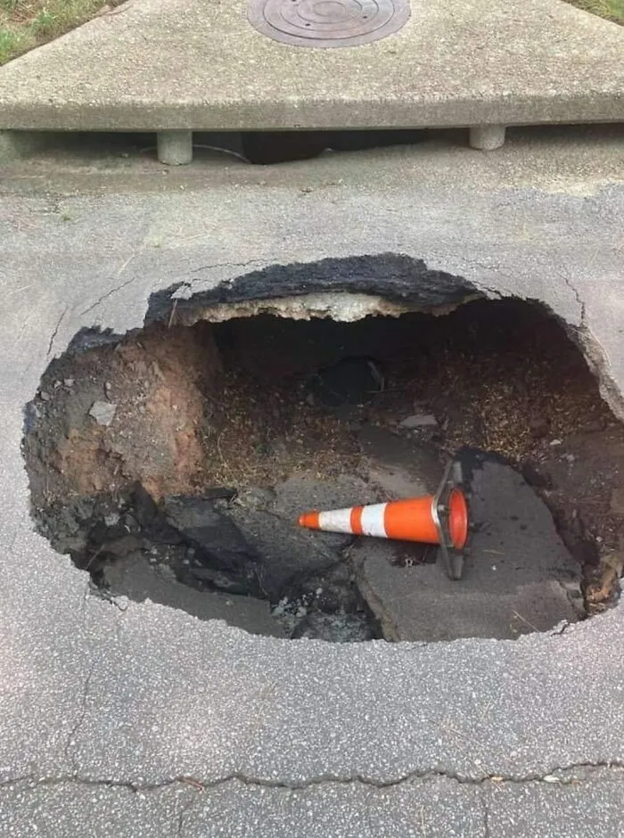 A traffic cone in a large pavement hole, highlighting disregard for OSHA safety regulations.
