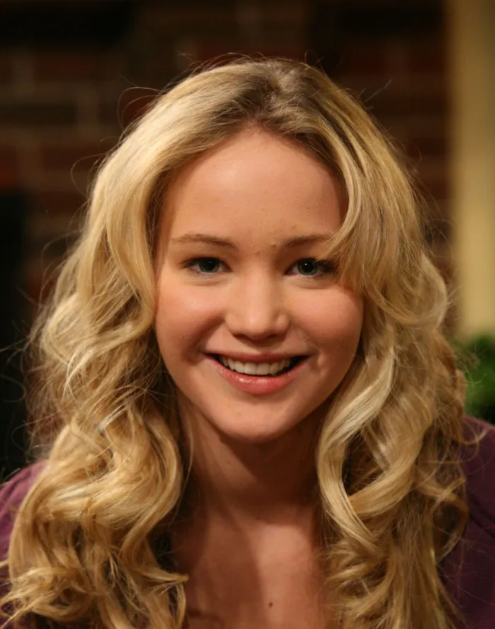 Young woman with curly blonde hair smiling, representing celebrities before they were famous revealing their true personality.