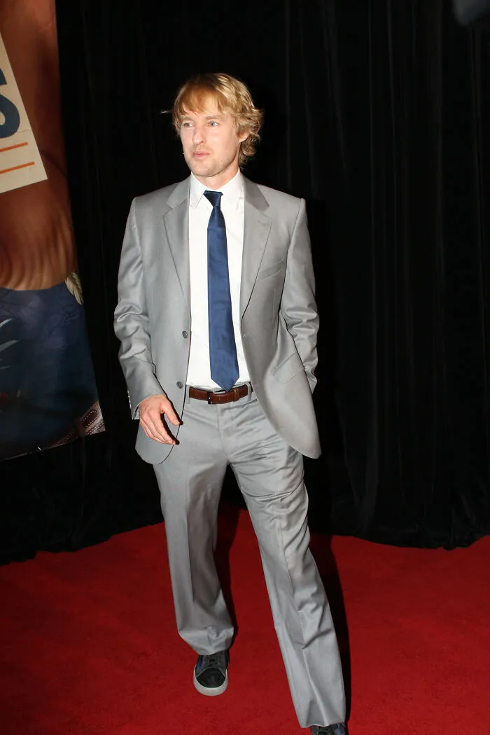 Blonde male celebrity in a gray suit and blue tie posing on a red carpet highlighting smartest celebrities.