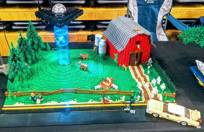 LEGO builds showcasing a farm scene with a red barn, cows, trees, and a light-up UFO in a detailed diorama setting.