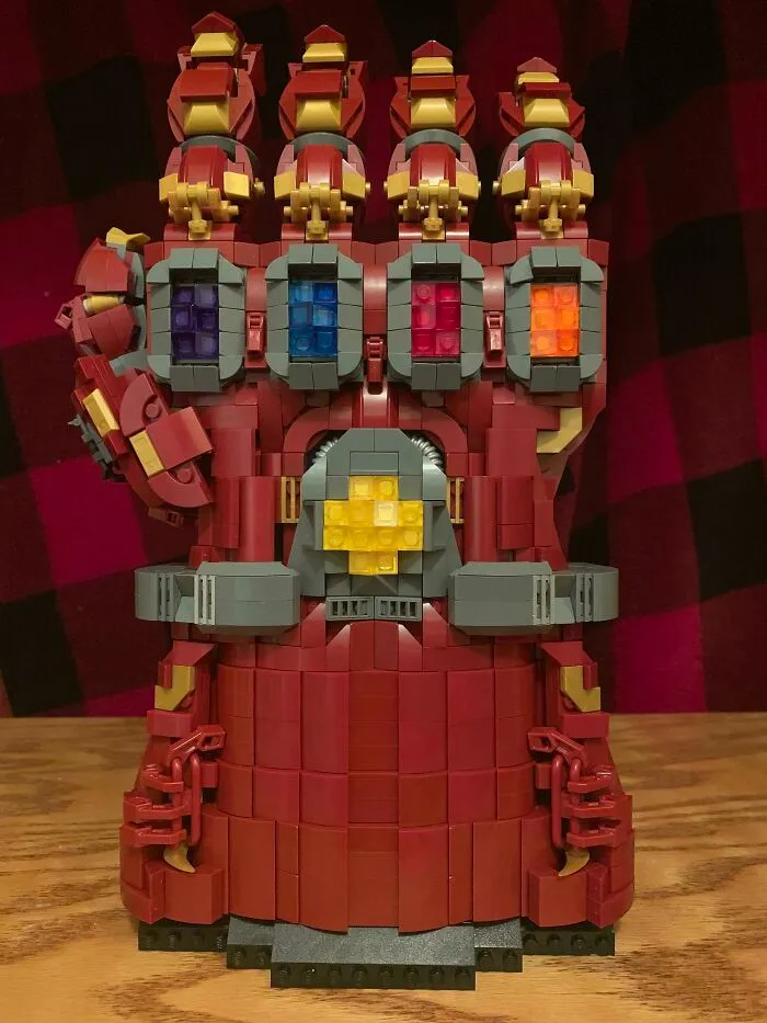 LEGO build of a detailed red gauntlet with colorful blocks, showcasing incredible LEGO art on a wooden surface.