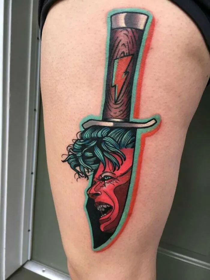 Psychedelic art tattoo featuring a colorful dagger on thigh with a vibrant face design.