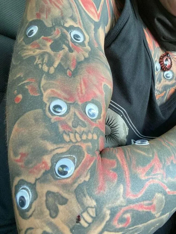 Psychedelic tattoo featuring skulls with googly eyes, vibrant red and black ink on an arm.