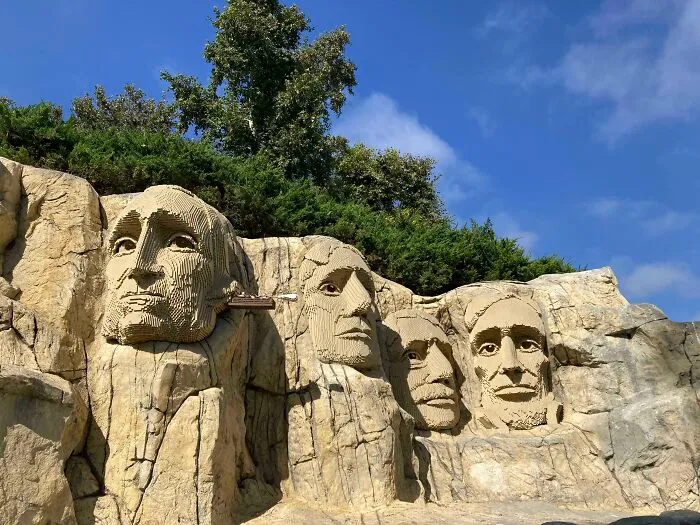 LEGO builds recreating Mount Rushmore with intricate details under a bright blue sky and green trees.