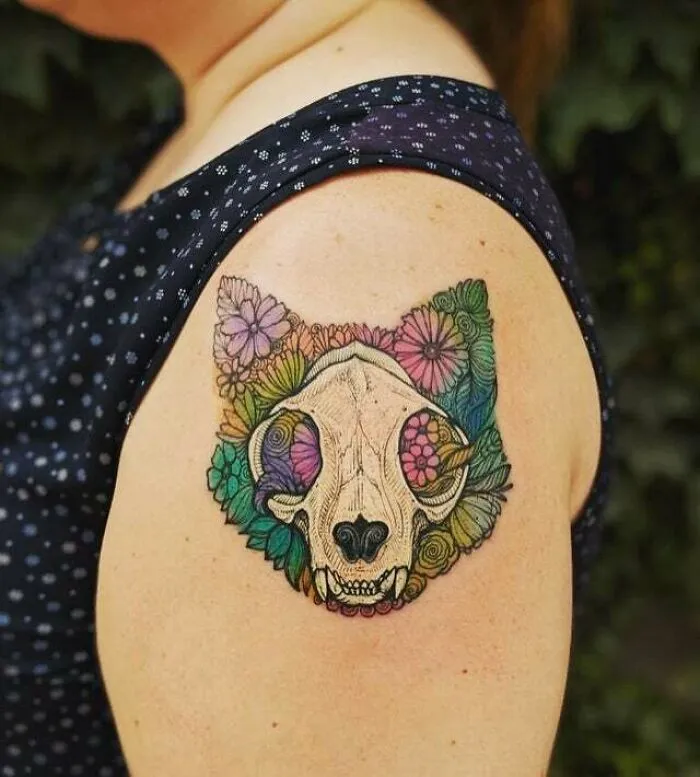 Colorful psychedelic tattoo of a wolf skull with floral patterns on upper arm.