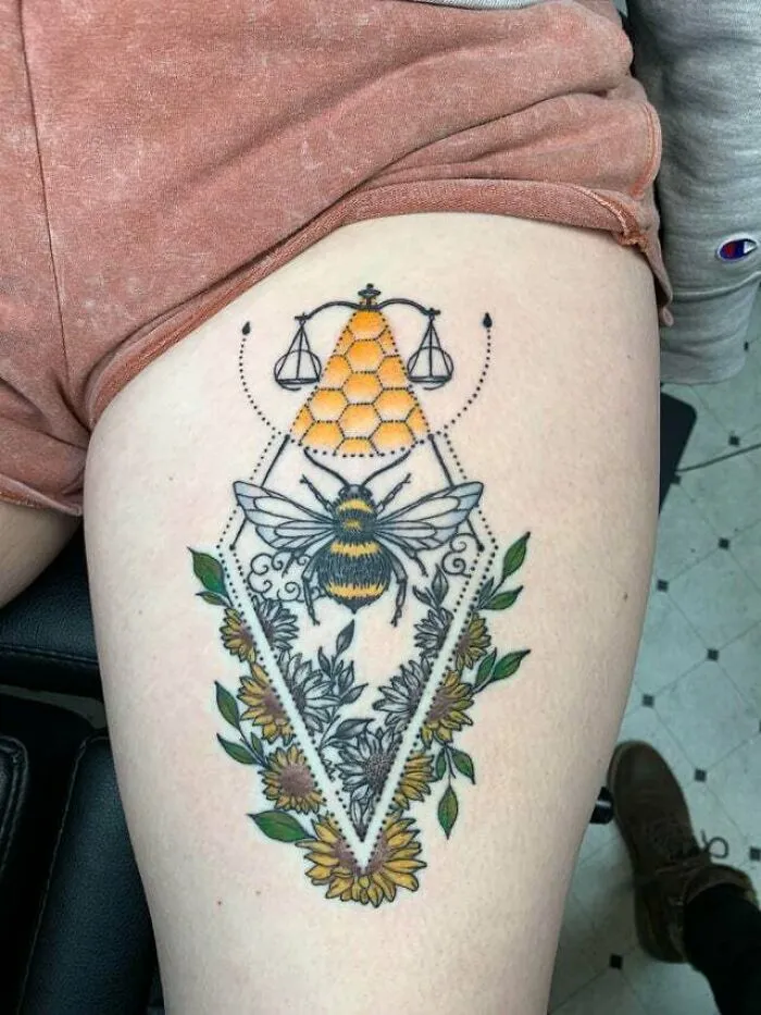 Psychedelic art tattoo of a bee with honeycomb and flowers on a person's thigh.