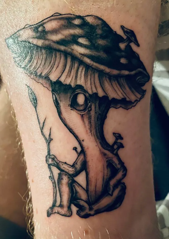 Trippy tattoo of a whimsical mushroom character holding a branch.
