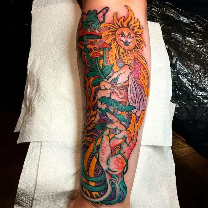 Colorful trippy tattoo of a fairy with mushrooms, sun, and frogs on an arm sleeve.