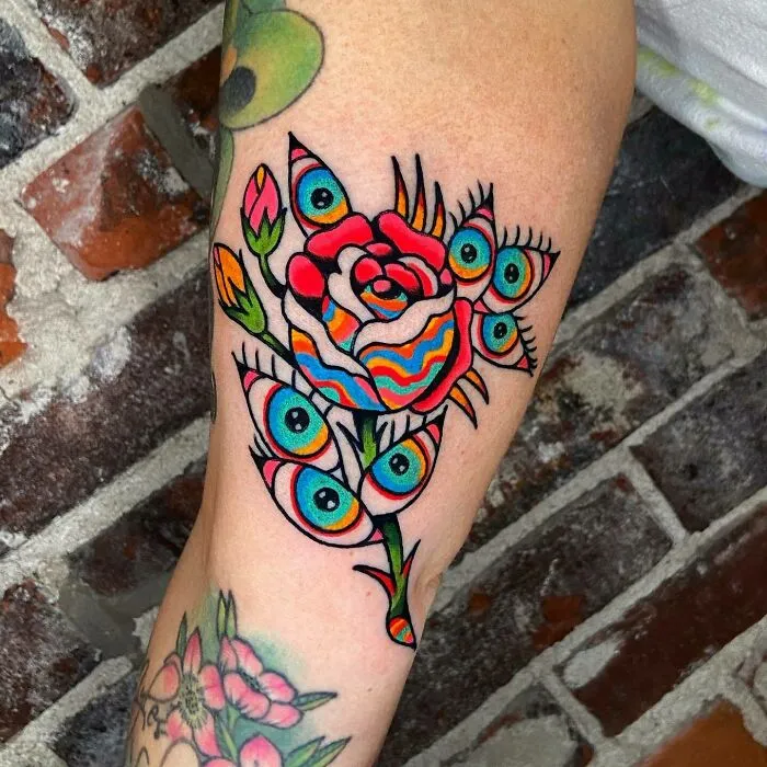 Colorful trippy tattoo of a rose with psychedelic eyes and patterns on an arm.