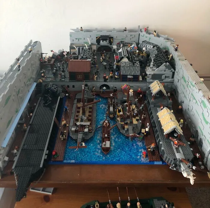 Intricate LEGO builds depicting a detailed medieval harbor scene with ships, buildings, and minifigures in a walled fortress.