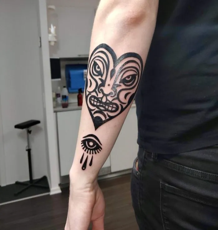 Angry heart with face and eye tattoo on arm, showcasing trippy tattoo art.