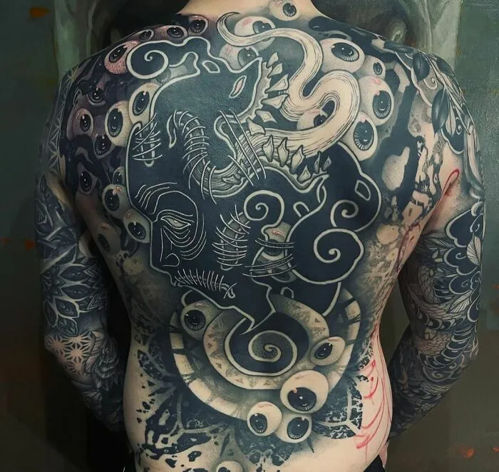 Full back tattoo with trippy eyes and octopus design, blending intricate patterns in a surreal style.