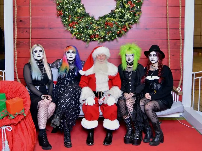 Santa posing with four goth individuals in a humorous Christmas scene under a festive wreath.