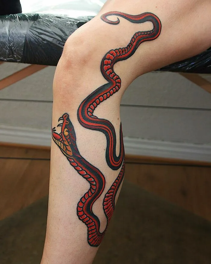 Snake design trippy tattoo on a leg, featuring bold red and black patterns.