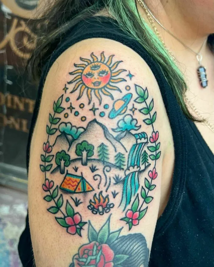 Colorful trippy tattoo featuring a sun, mountains, waterfall, and camping scene on an arm.