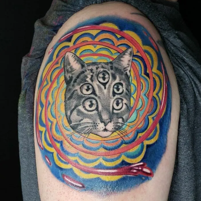 A psychedelic tattoo of a cat with multiple eyes, surrounded by colorful, trippy patterns.