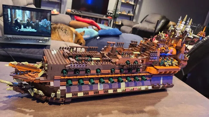 Detailed LEGO build of a large ship displayed on a table in a cozy living room setting with a laptop nearby.