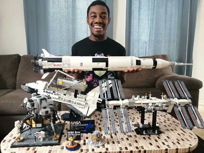Man holding a detailed LEGO rocket with a space shuttle and space station LEGO builds displayed on table, showcasing incredible LEGO builds.