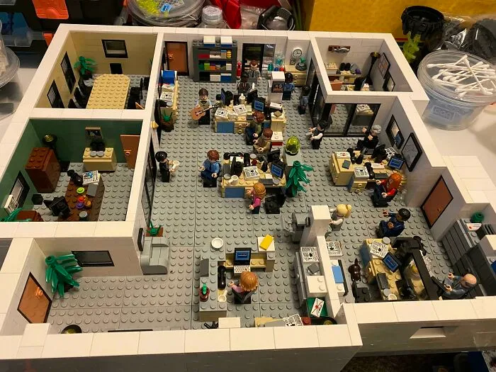 LEGO builds of an office workspace with miniature figures at desks, computers, and detailed decorations showcasing incredible creativity.