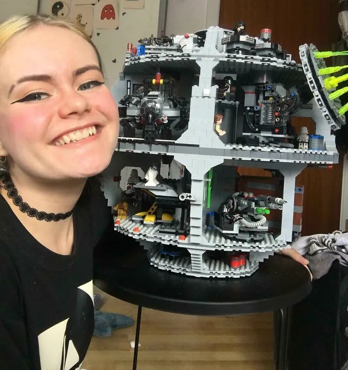 Smiling person posing with an intricate LEGO build resembling a detailed multi-level spaceship model on a black table.