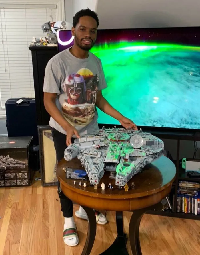 Man displaying an incredible LEGO build of a Millennium Falcon on a round table in a living room setting.