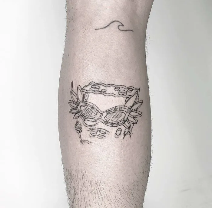 Trippy tattoo of a character with glasses and floral elements on a person's leg, featuring minimalist abstract lines.
